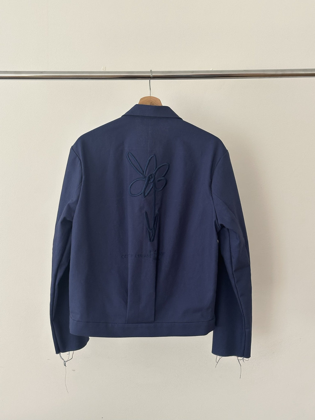 Atelierjacke Dunkelblau am Holzbügel, Rücken mit Blume Ton in Ton