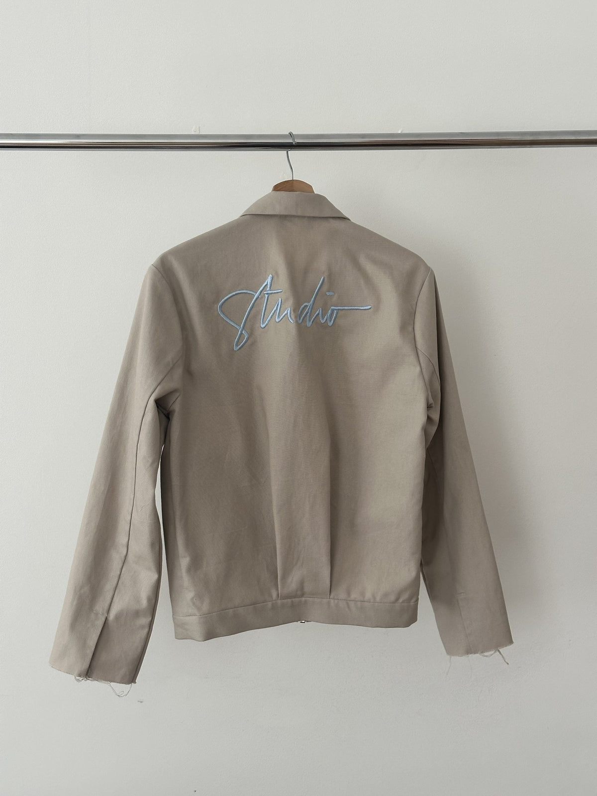 Atelierjacke Hellgrau am Holzbügel, Rücken mit Schriftzug „Studio“