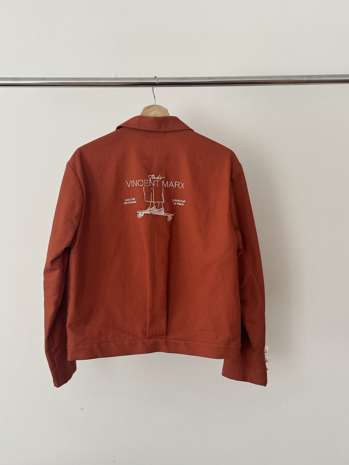 Atelierjacke Rostorange am Holzbügel, Rücken mit Skateboard-Stickerei